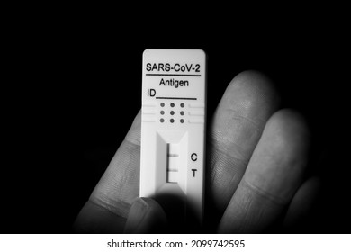 Hand holding a positive Covid-19 antigen test against black background. Monochrome image.
