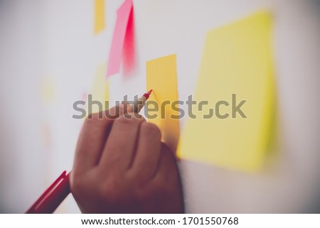 The hand is holding the post it notes attached to the wall. Concept brainstorming, share idea.