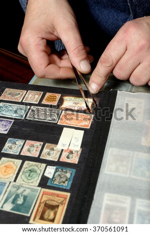 Hand holding postage stamp with tweezers over album