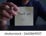 A hand holding a post-it note, writing a thank you message. Expressing kindness to coworkers, loved ones.