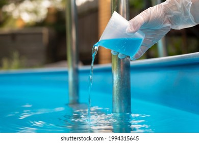Hand holding and pouring algicide blue liquid from glass into water of swimming pool. Water purification and prevention of appearance of algae and microorganisms. - Shutterstock ID 1994315645