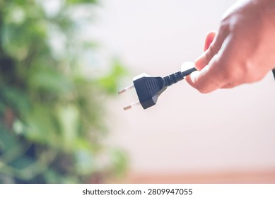 Hand holding a power plug cable, disconnecting power and symbolizing electricity consumption reduction, cost savings, energy efficiency, and environmental conservation