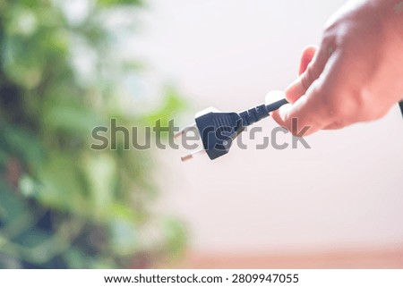 Hand holding a power plug cable, disconnecting power and symbolizing electricity consumption reduction, cost savings, energy efficiency, and environmental conservation