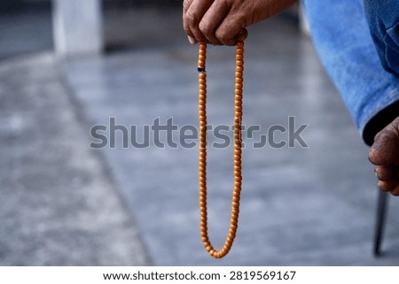 Hand Holding Prayer Beads for Islamic Dhikr
Close-up of a Muslim man's hand holding traditional wooden prayer beads (tasbih) while performing dhikr and Islamic prayer in a peaceful setting.                            
