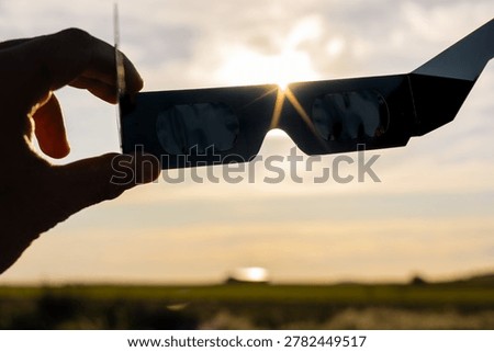Hand holding protective solar eclipse glasses, safely viewing the glowing sun and celestial event against a hazy sky