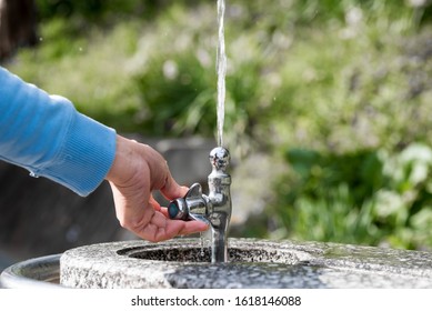 A Hand Holding A Public Drinking Fountain. Water Coming Out Splashing Upward. 