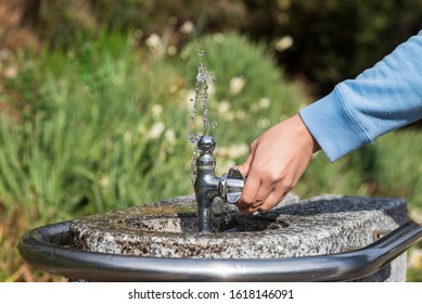 A Hand Holding A Public Drinking Fountain. Water Coming Out Splashing Upward. 