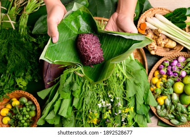Hand holding purple sticky rice wrapped by banana leaf and fresh organic Asian vegetables from local farmer market, Northern of Thailand