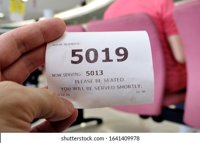 Hand Holding A Queue Number Ticket For A Counter Service At A Bank While Waiting Turn To Be Attended To. A Queue Ticket Showing The Current Waiting Number Been Assigned.