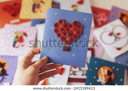 Hand holding quilling card with red heart balloon. Happy valentine day. woman making greeting cards. Hand made of paper quilling technique. Hobby, home office. Heart from red paper ribbons