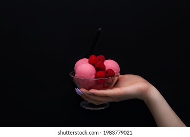 Hand is holding Raspberry ice cream in the transparent bowl on the black background . High quality photo