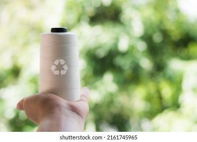 Hand holding Raw White Polyester FDY Yarn spool, Polyester Filament Yarn spool.PET fiber Yarn,spun polyester sewing thread with blurred green background. Recycle icon, sustainable icon and Bottle icon