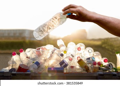 Hand holding recyclable plastic bottle in garbage bin environment conceptual.