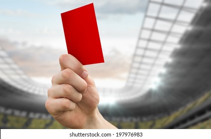 Hand Holding Up Red Card Against Football Stadium