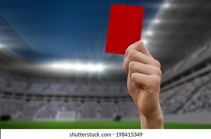 Hand Holding Up Red Card Against Football Stadium