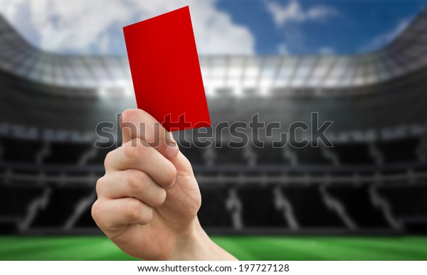 Hand holding up red card against large football\
stadium with empty stands