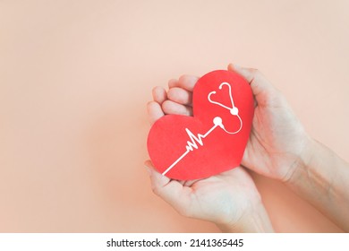 hand holding red heart with heartbeat and stethoscope icon on grunge orange pastel background for health check up concept including copy space