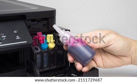 Hand holding red ink cartridge inject printer at home office.  