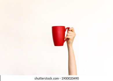 Hand Holding A Red Mug Of Coffee On Clean White Wall Background.