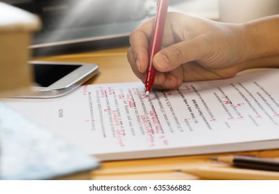 hand holding red pen over proofreading text in office