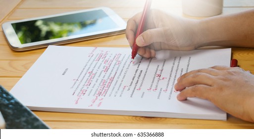 hand holding red pen over proofreading text on table