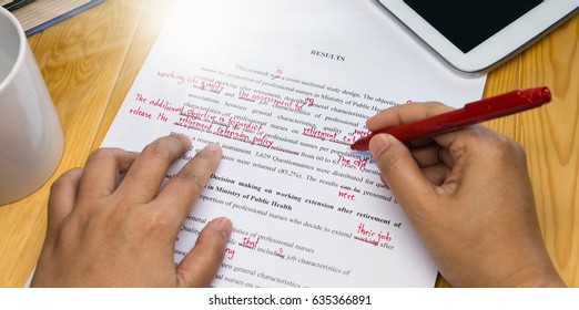 hand holding red pen over proofreading text on table - Shutterstock ID 635366891