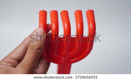 A hand holding a red plastic fork. The fork is bent and has a curved design. Concept of playfulness and creativity, as the fork is not a typical utensil but rather a fun and unconventional object