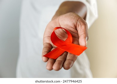 A hand holding a red ribbon, symbolizing AIDS and HIV awareness, raising support and promoting solidarity with those affected by the illness. - Powered by Shutterstock