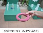 Hand holding a red rubber ring for throwing rings in throwing rings where players can throw green and blue rings into a white stick. Players help each other to throw as many rubber rings down the pole