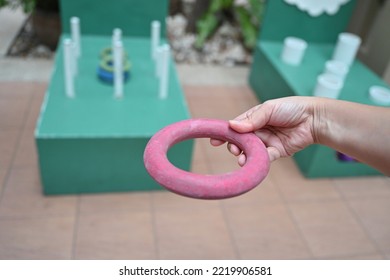 Hand holding a red rubber ring for throwing rings in throwing rings where players can throw green and blue rings into a white stick. Players help each other to throw as many rubber rings down the pole