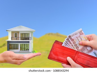 Hand holding red wallet with Thai money banknote and miniature house on a blur green field blue sky background - Shutterstock ID 1088543294