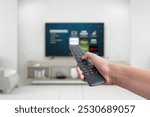 Hand holding a remote control for a smart TV, featuring app buttons for streaming services. Concept of versatile entertainment, showcasing the functionality of smart TVs