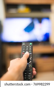 Hand holding remote control with television background in a living room