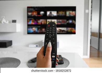 Hand holding a remote controller with a streaming website on TV in the blurred background, selective focus.