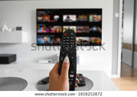 Hand holding a remote controller with a streaming website on TV in the blurred background, selective focus. Stock fotó © 