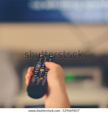 Hand holding remote tv controller towards televison