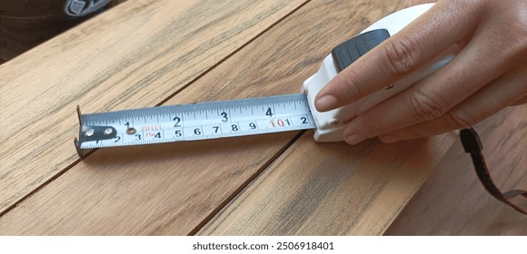 Hand holding a retractable black and yellow measuring tape set at a distance of 10 cm, on a wooden background, a useful tool for measuring length, width and height. - Powered by Shutterstock