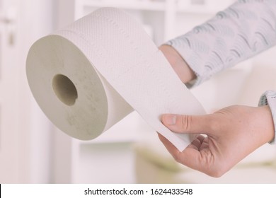 Hand holding a roll of toilet paper at home