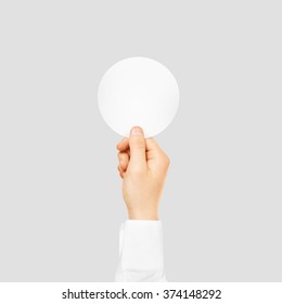 Hand holding round blank white sticker mock up isolated on gray. Sticker mockup holder. Empty paper clue remnder hold in hands. Arm sticking round sticker.