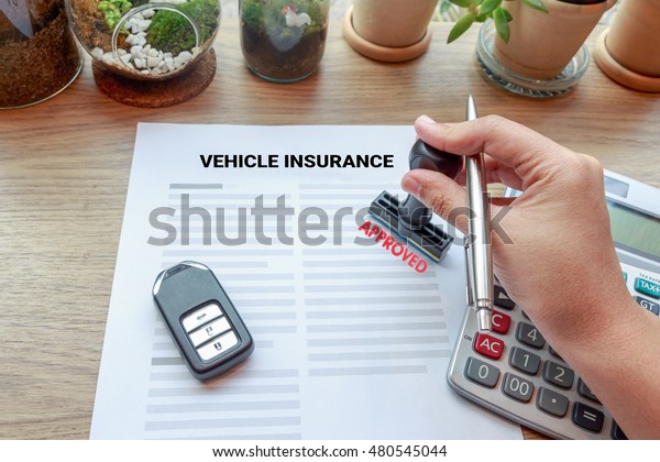 Hand holding rubber stamp with approved\
vehicle insurance, car key and\
calculator.