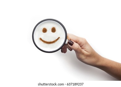 Hand holding rustic white mug and coffee cream  Food art creative concept image  happy face drawing and cinnamon powder over white background 