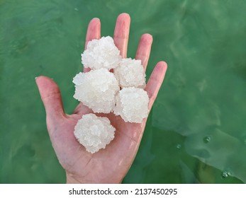 Hand Holding Salt From The Bottom Of The Dead Sea Held Up Against The Bright Green Sea Water