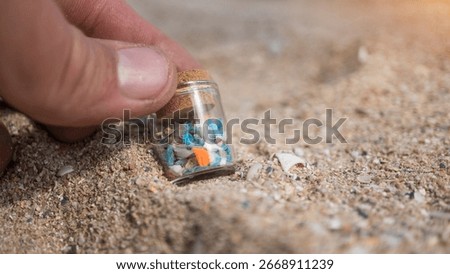 A hand holding a sample jar with tiny plastic particles collected from the seashore, illustrating the environmental crisis and water contamination. Microplastic pollution on the beach.