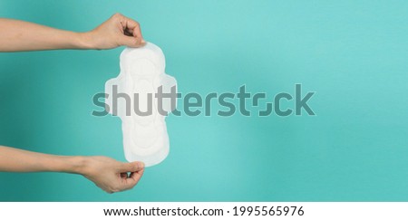 Hand is holding Sanitary napkin  ongreen mint or tiffany blue background.