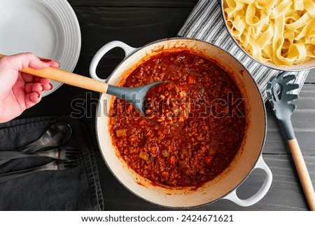 Hand Holding a Serving Spoon of Authentic Bolognese Sauce: Ragu alla bolognese Italian tomato and meat sauce in a spoon held over a large pot