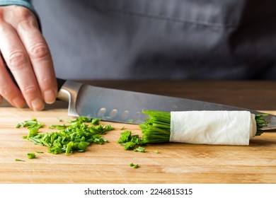 A hand holding a sharp knife in behind a pile of freshly chopped chives. - Powered by Shutterstock