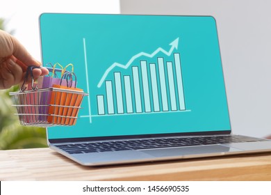 Hand holding shopping basket on laptop keyboard with graph growth and increase of chart on screen. Consumer can buy product directly anywhere anytime from seller. Online shopping and ecommerce concept - Shutterstock ID 1456690535