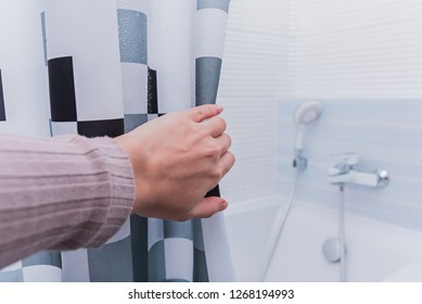 Hand Holding Shower Curtain In White Bathroom.