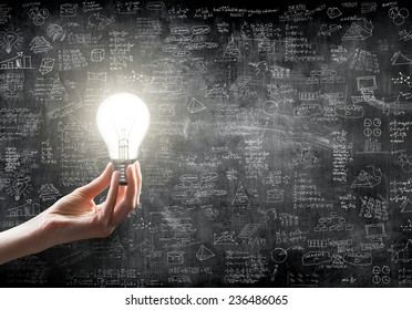 hand holding or showing a light bulb in front of  business idea concept on wall backboard blackground