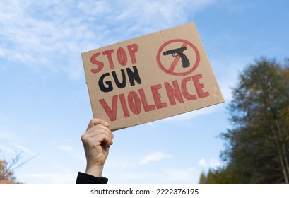 Hand holding a sign with slogan Stop Gun Violence and black pistol strikethrough. Woman with placard at protest rally demonstration strike to ban weapons and end shooting.